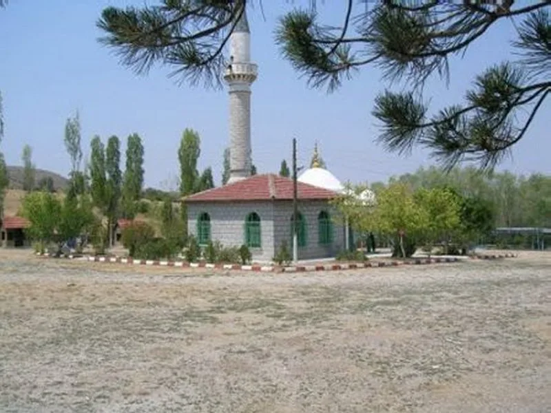 Hoşislamlar ziyaret alanındaki taş duvarlı yapı, minare ve çevredeki ağaçlar